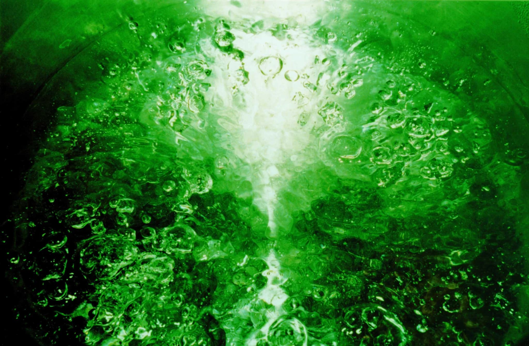 Abstract photograph in deep green: a bright vertical column of light rising through a field of bubbles.